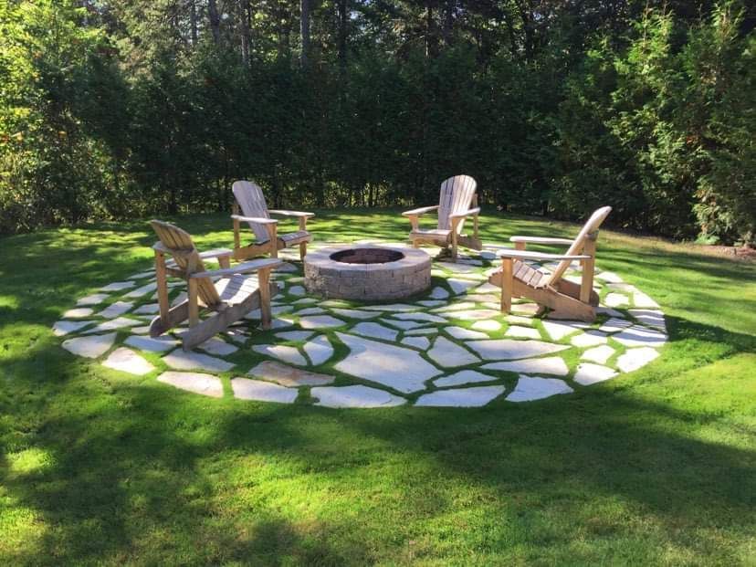 Un foyer au milieu d'une pelouse avec des chaises autour.