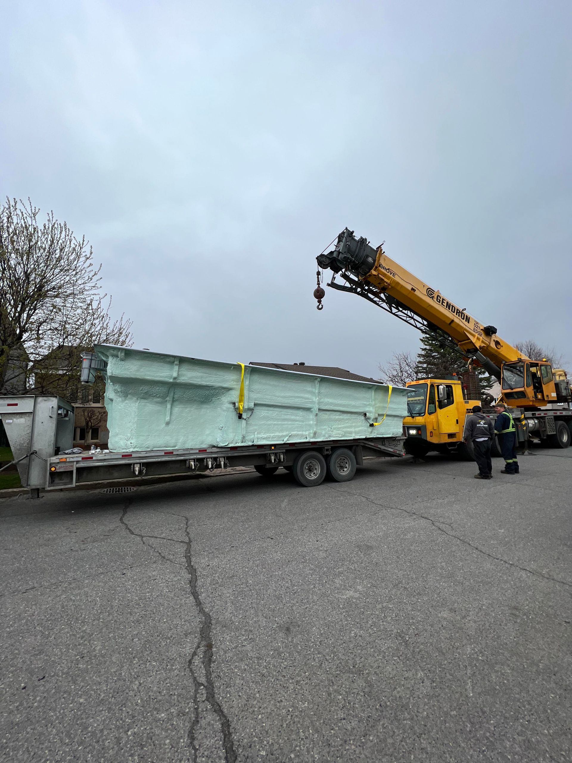 Une grue jaune soulève un gros morceau de métal sur un camion.