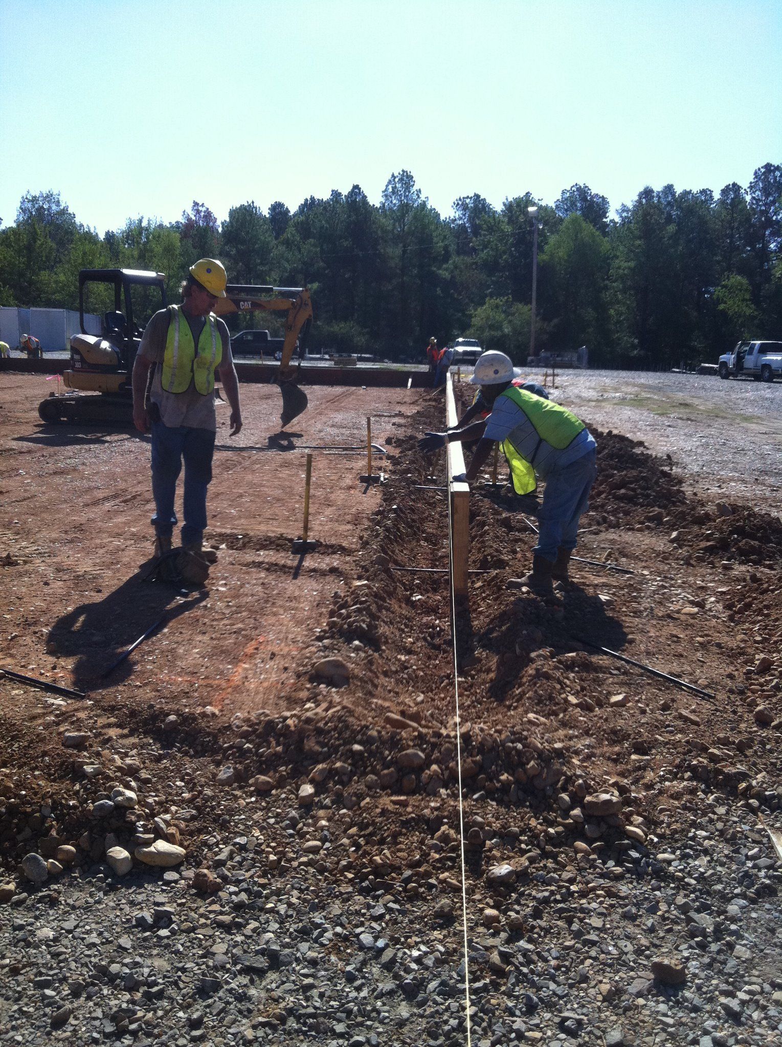 Two construction workers setting up stakes on a dirt ground at a construction site.