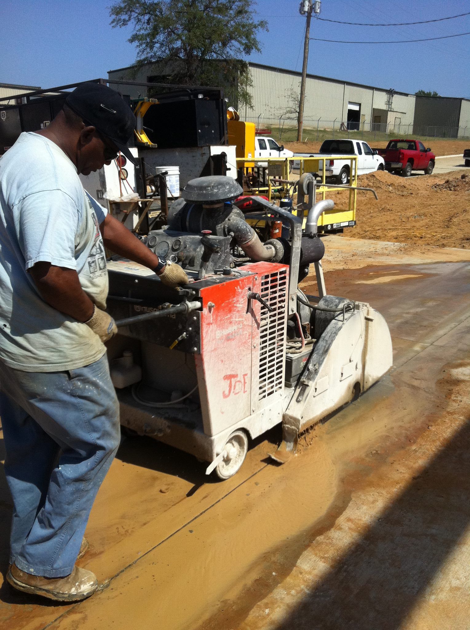 Person operating a concrete saw to cut a line in a concrete surface.