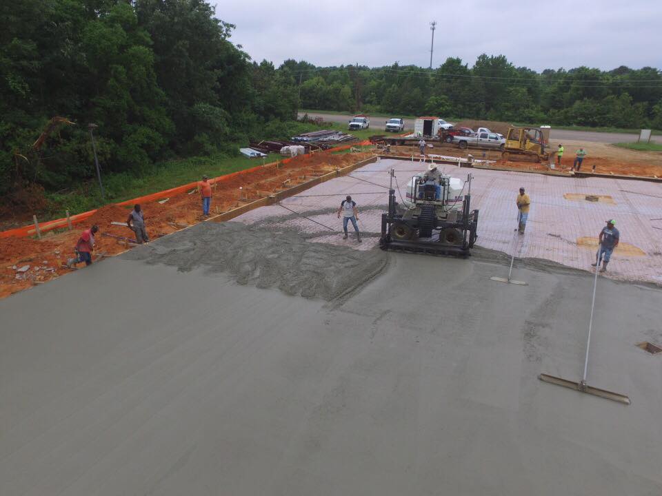 Construction workers smoothing wet concrete on a large paved area with machinery and tools. Overcast day.