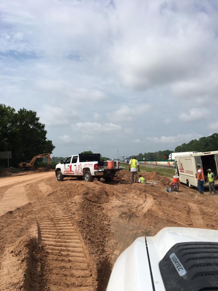 Construction site: White truck, workers in high-vis vests, trailer, dirt road, cloudy sky.