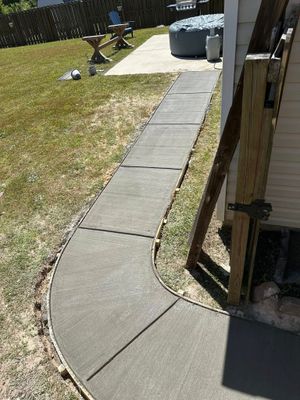 Concrete walkway curves toward patio, grass on left, wooden structure on the right.