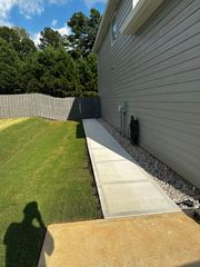 Concrete ramp leading from a house to the yard. Gray siding, gravel bed, and wooden fence visible.