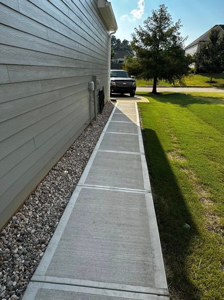 Sidewalk next to house with gray siding. A black truck is parked in the distance.