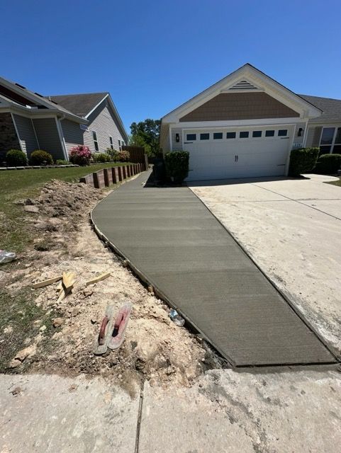 Newly poured concrete sidewalk leading from driveway to house, sunny day.