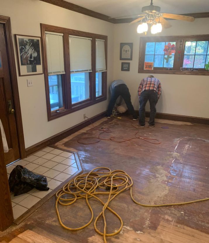 Two men are working on a wooden floor in a room with a ceiling fan