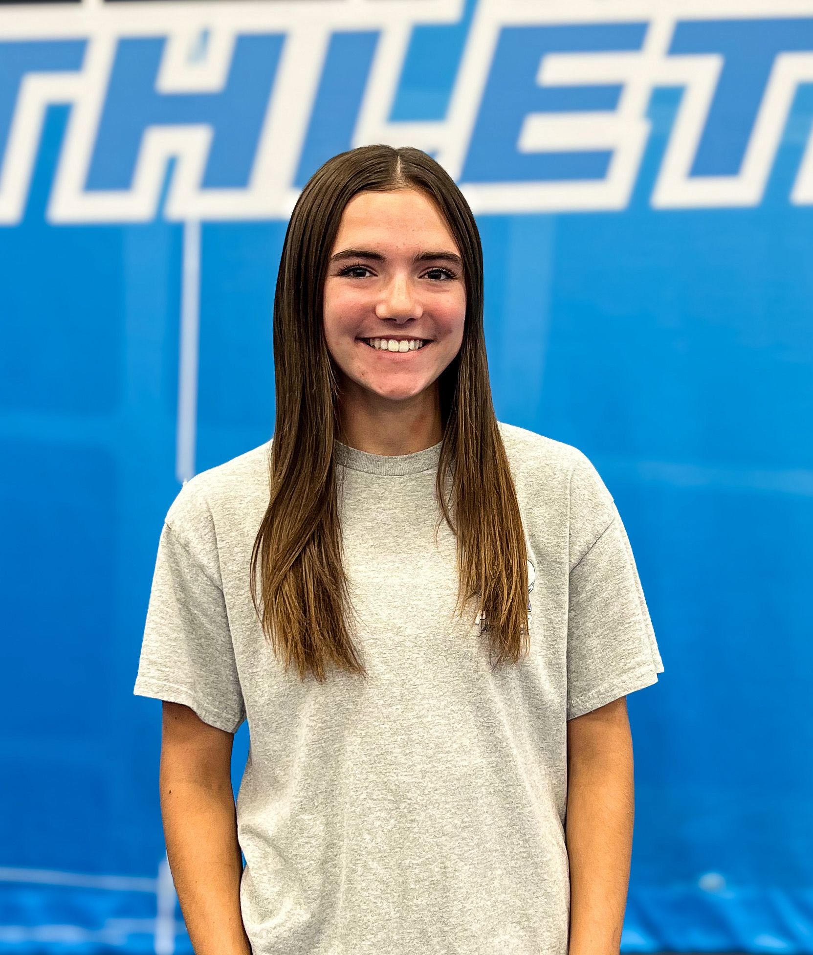 A young woman wearing a grey t-shirt is standing in front of a blue wall.