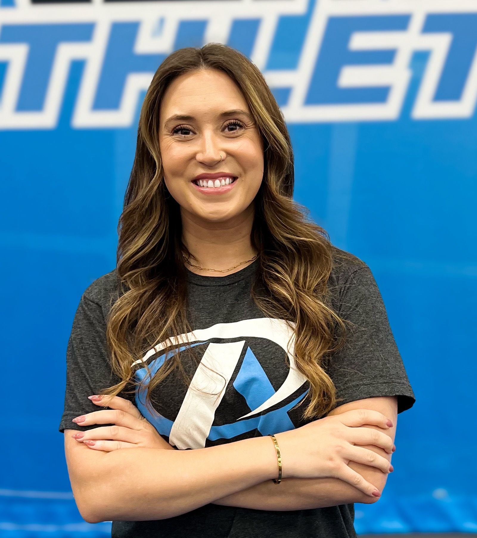 A woman is standing in front of a blue wall with her arms crossed and smiling.