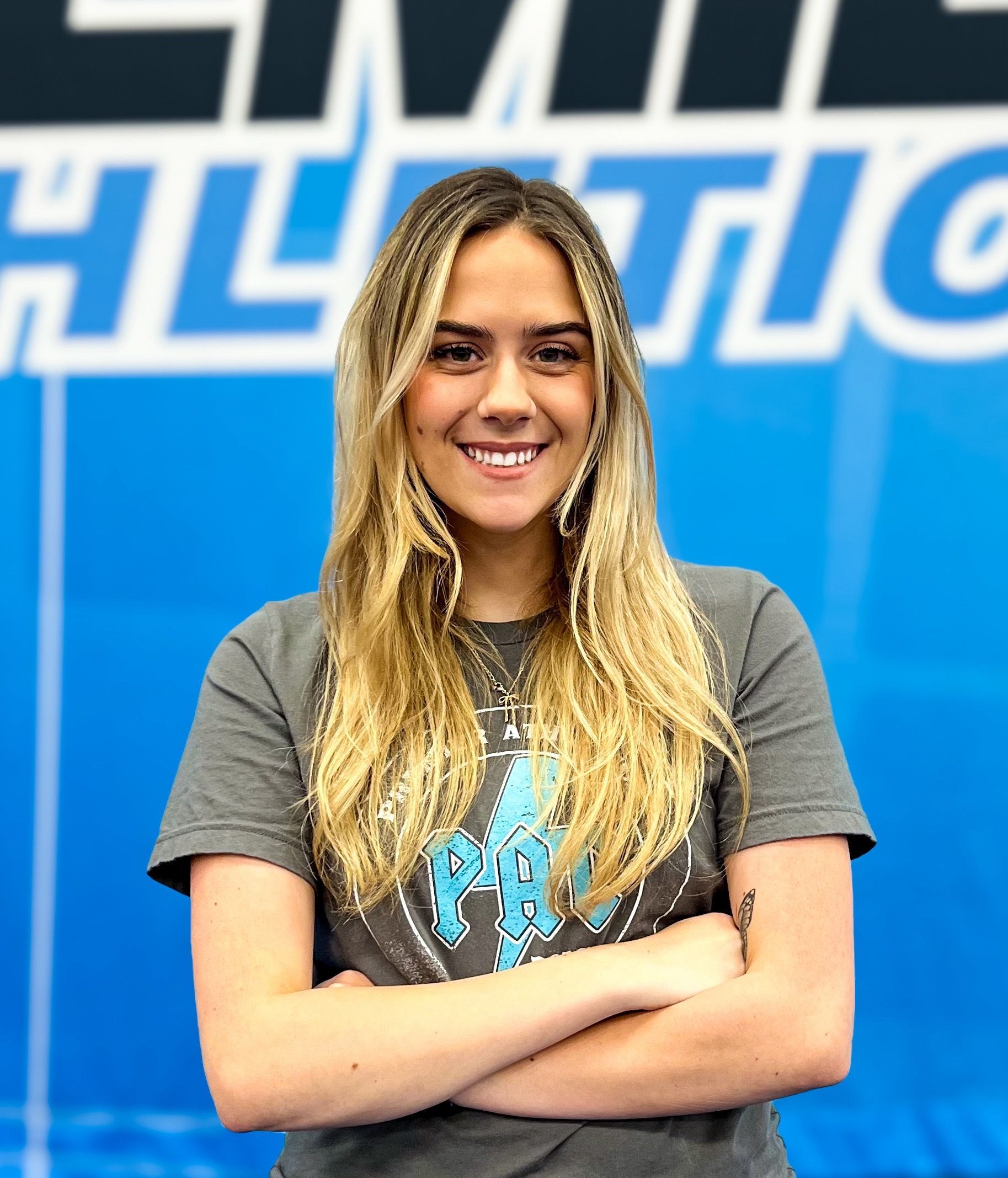 A woman is posing for a picture with her arms crossed in front of a sign that says athletic