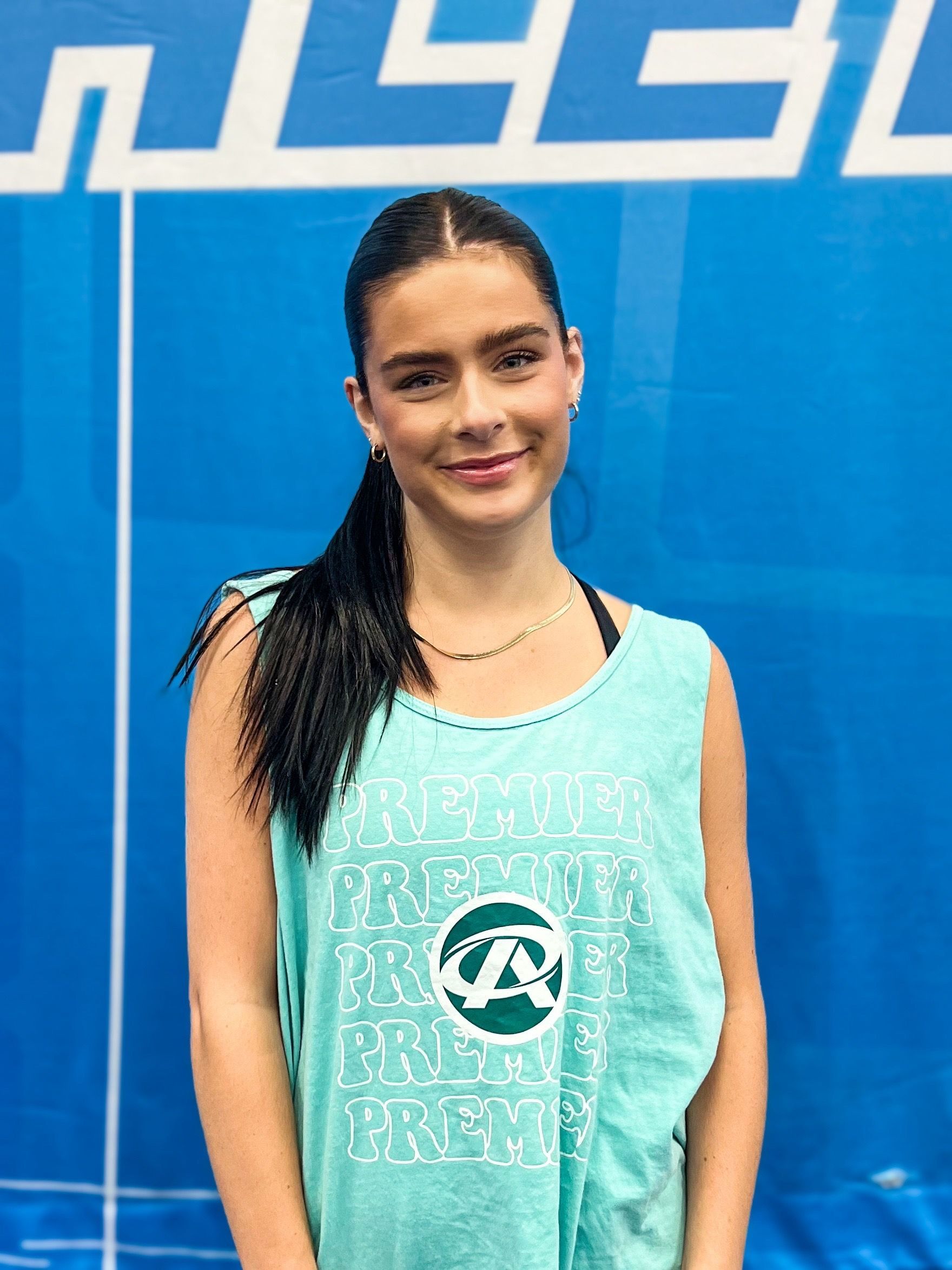 A woman in a green tank top is standing in front of a blue wall.