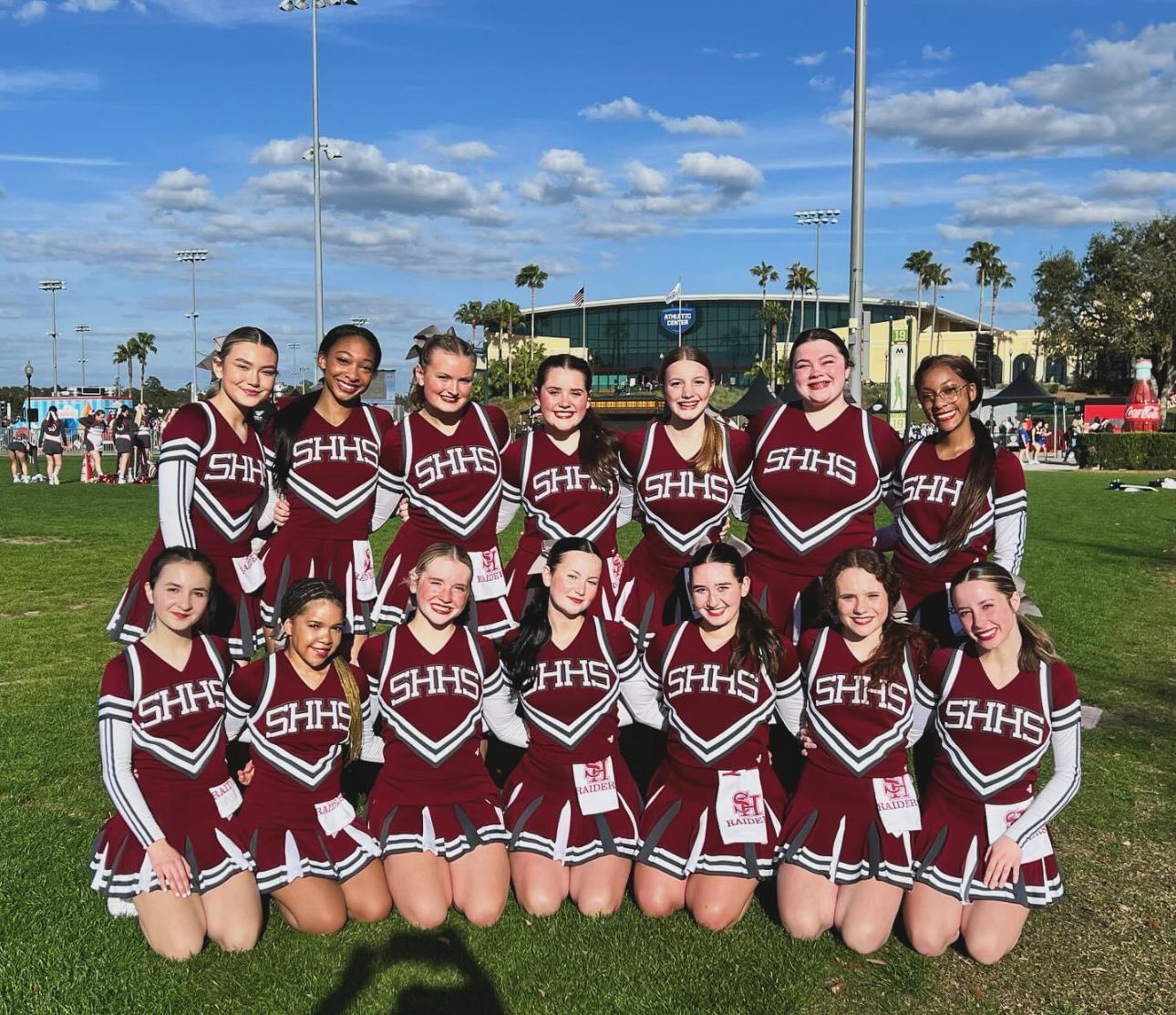 A group of cheerleaders are posing for a picture in a field.