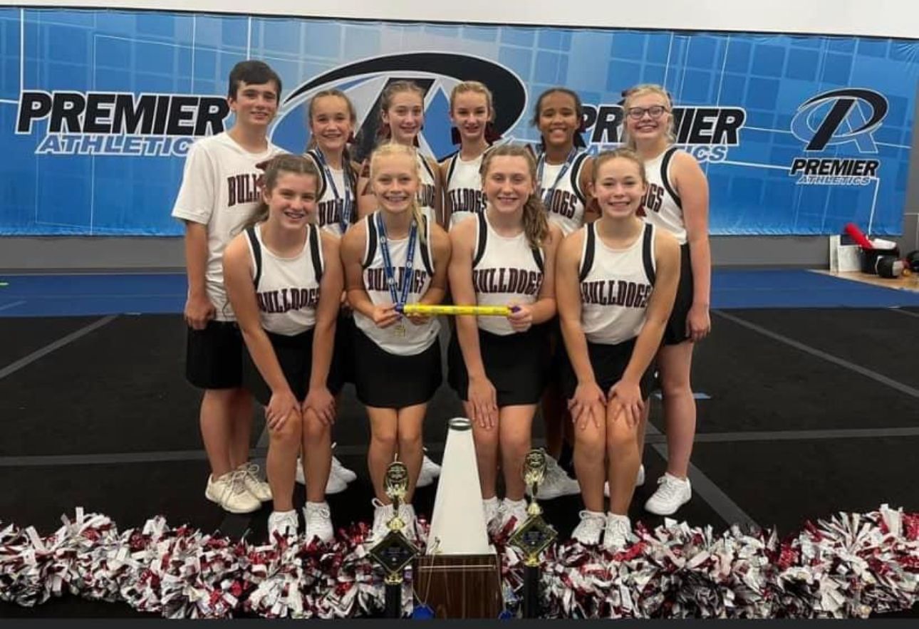 A group of cheerleaders are posing for a picture in front of a premier athletic sign