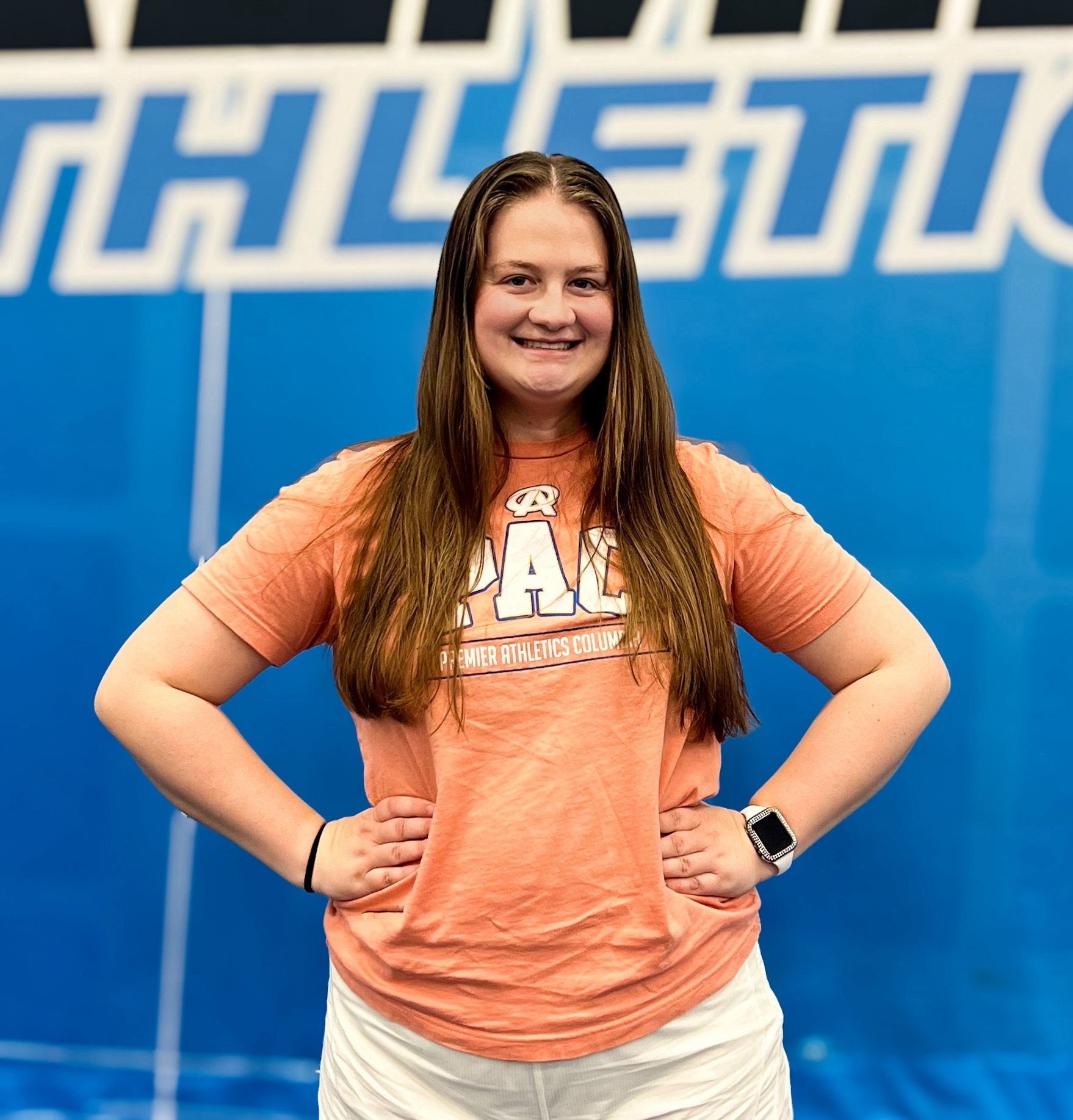 A woman is standing with her hands on her hips in front of a sign that says athletics