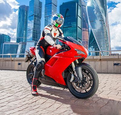 Person in white and red motorcycle gear on a red sport bike, city skyline in the background.