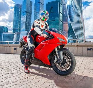 Person in white and red motorcycle gear on a red sport bike, city skyline in the background.