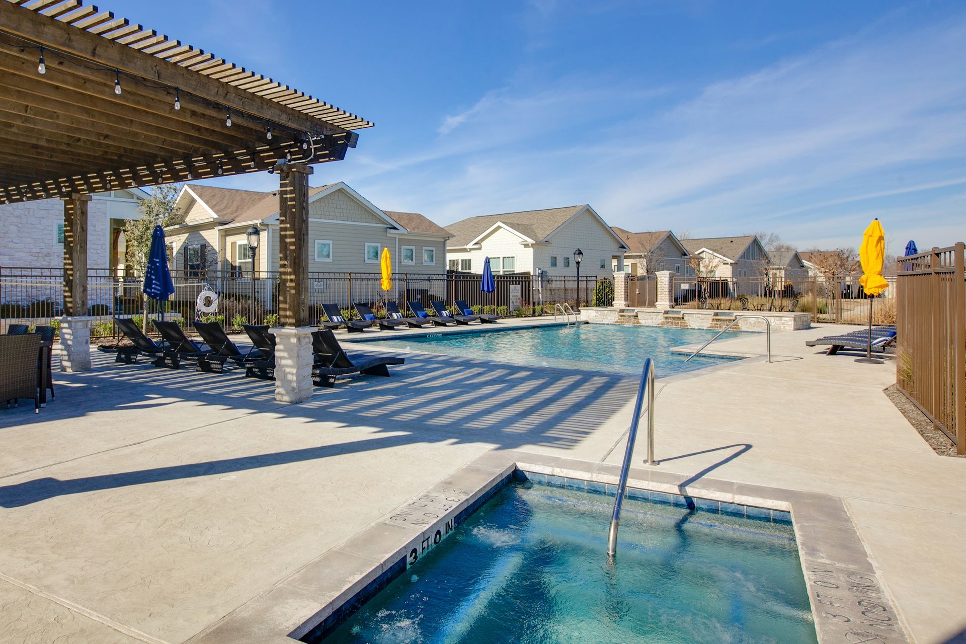 A large swimming pool surrounded by chairs and umbrellas in a residential area.