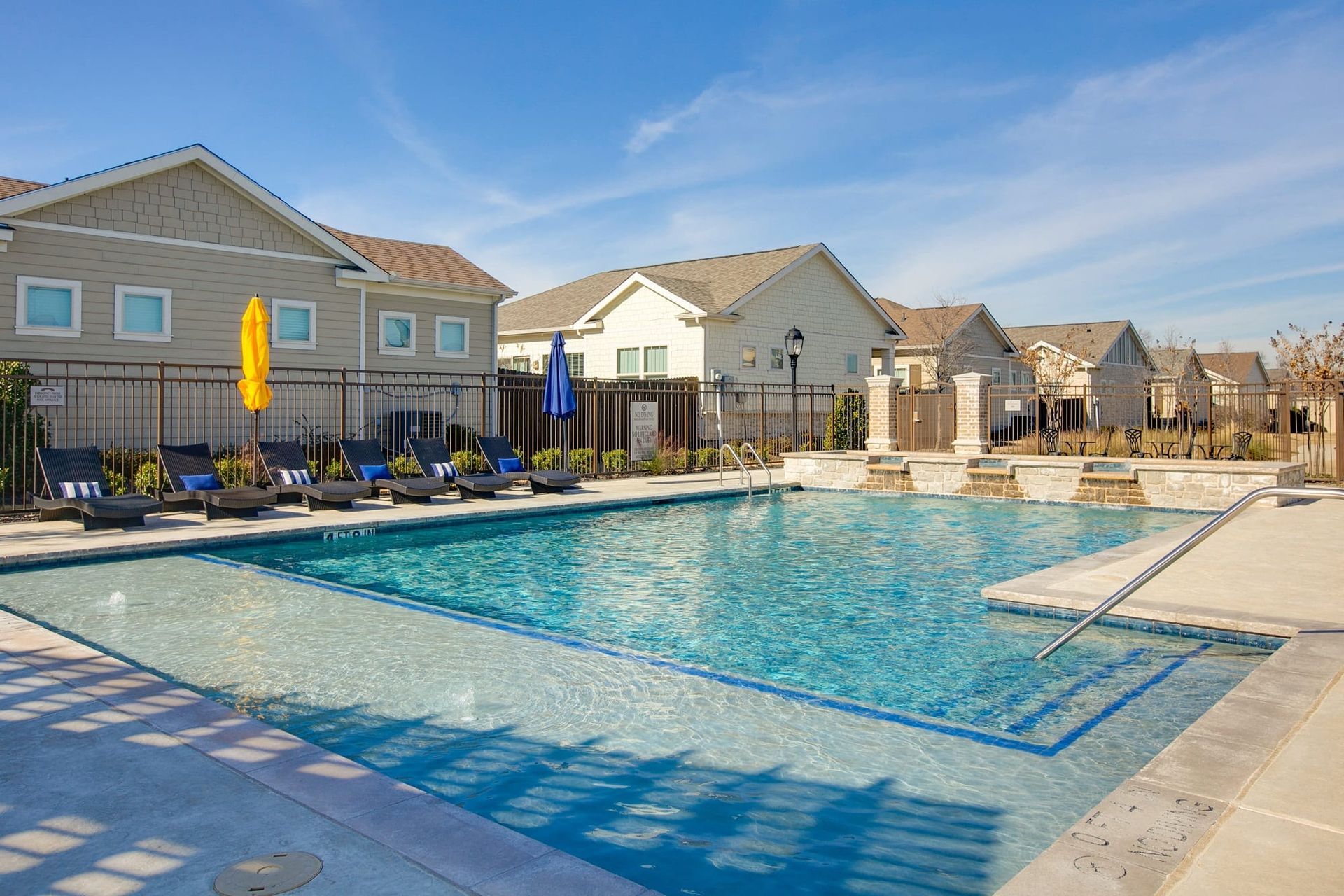A large swimming pool surrounded by chairs and umbrellas in front of a row of houses.