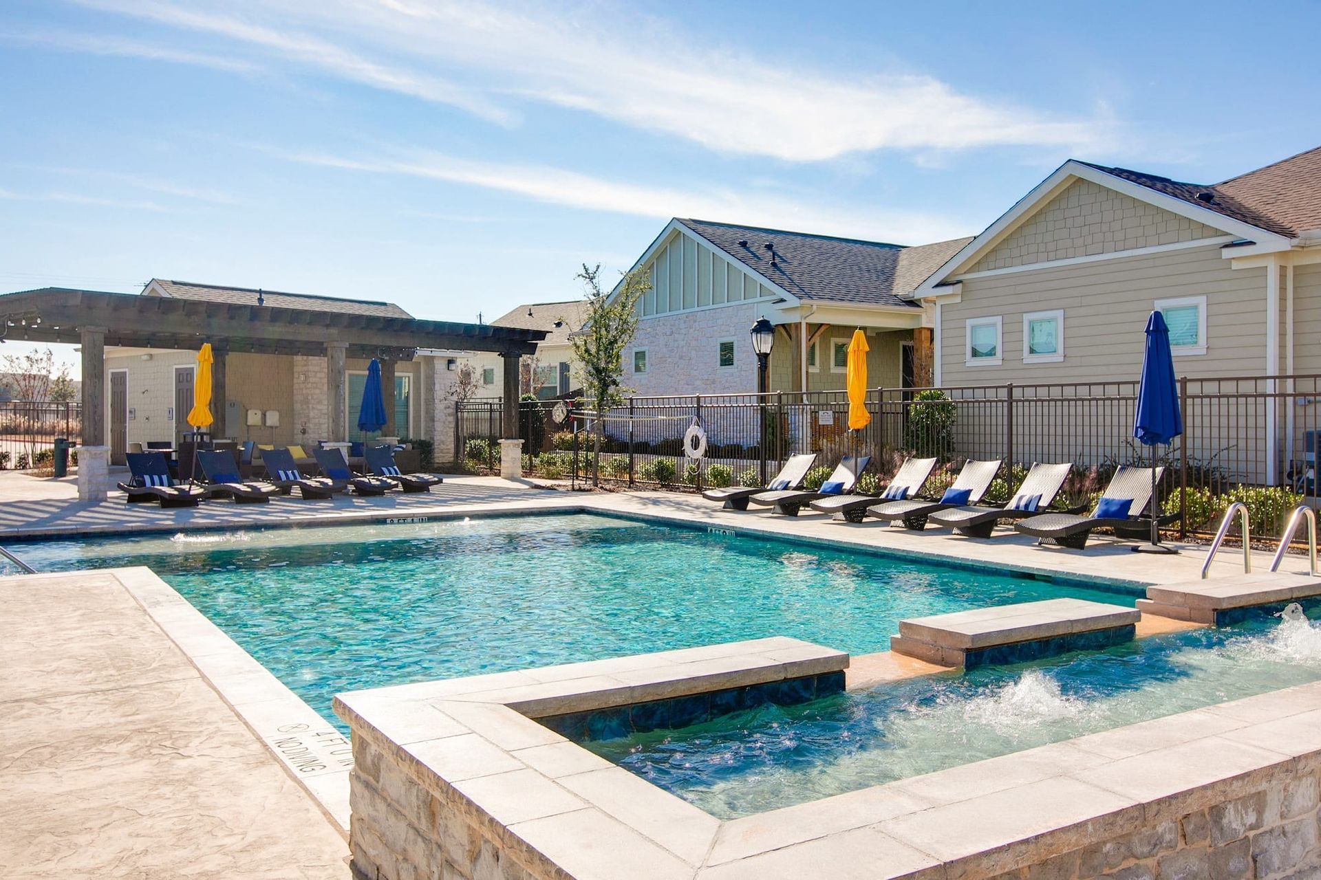 A large swimming pool surrounded by chairs and umbrellas in front of a house.