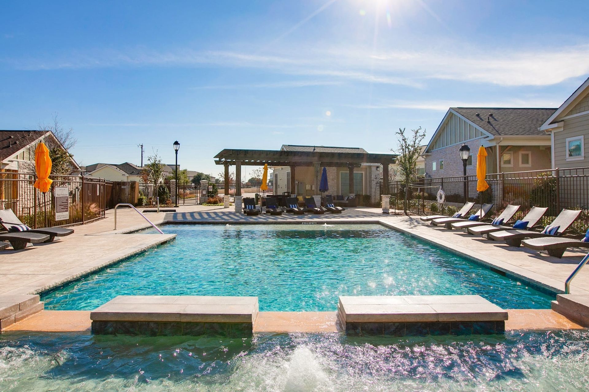 A large swimming pool surrounded by chairs and umbrellas in a residential area.
