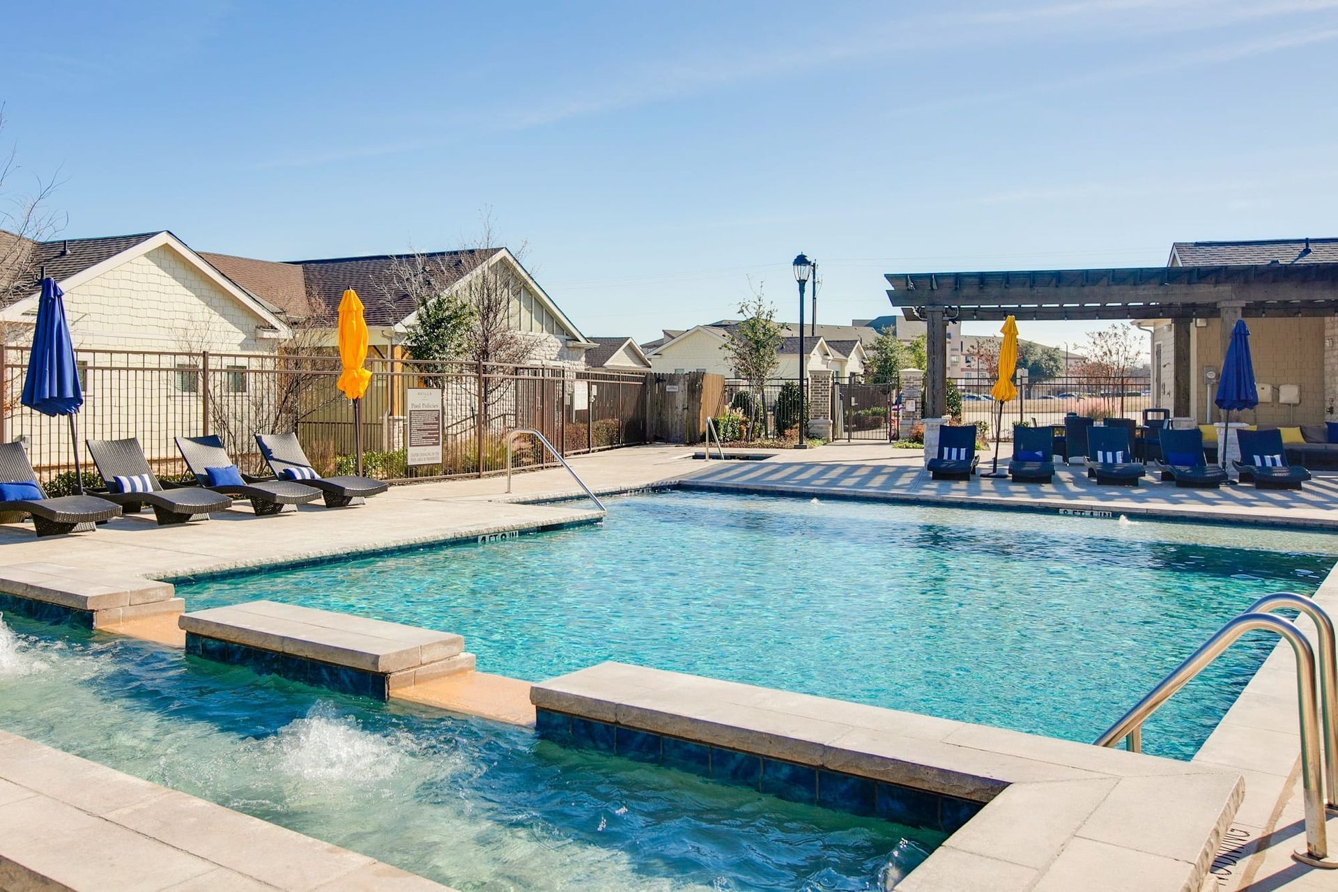 A large swimming pool surrounded by chairs and umbrellas in a residential area.