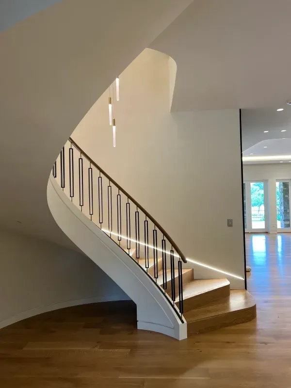 A curved staircase with wooden steps, a dark metal railing, and integrated under-rail lighting in a modern interior.