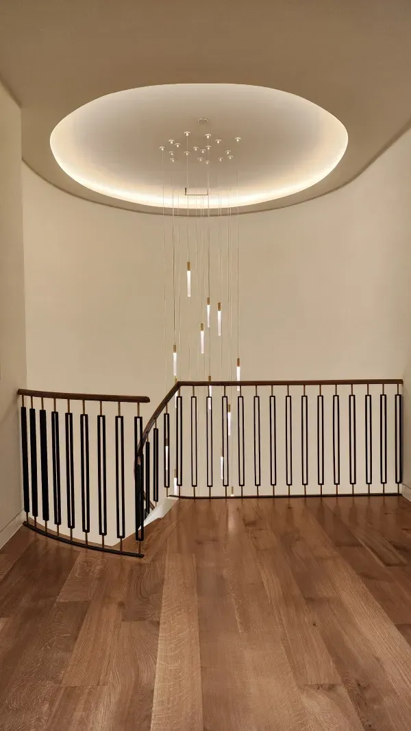 A curved staircase with black metal railings and wood floors, illuminated by a modern circular recessed light fixture.