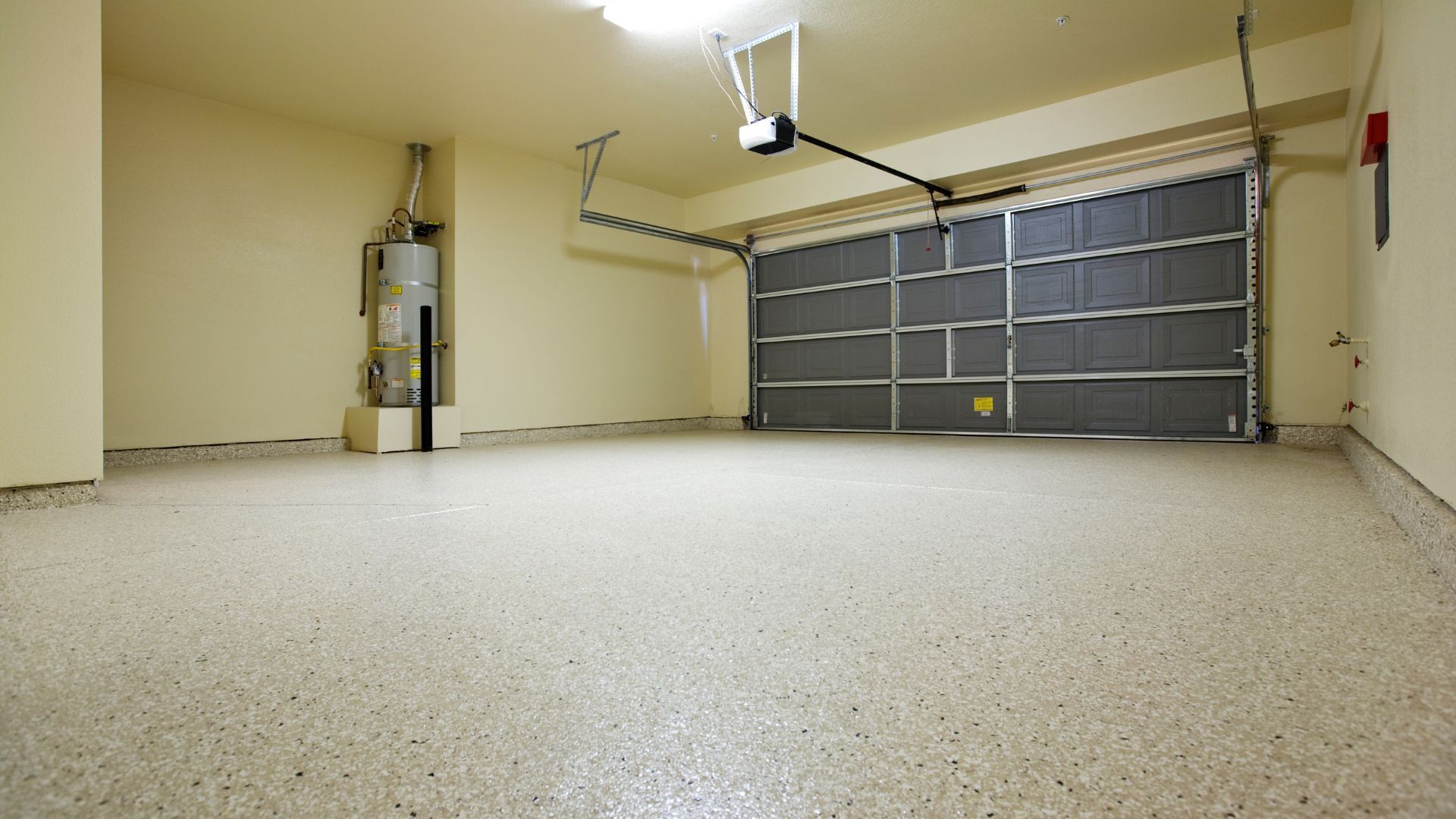 An empty, clean garage with light beige walls, a gray overhead door, and a speckled epoxy concrete floor.