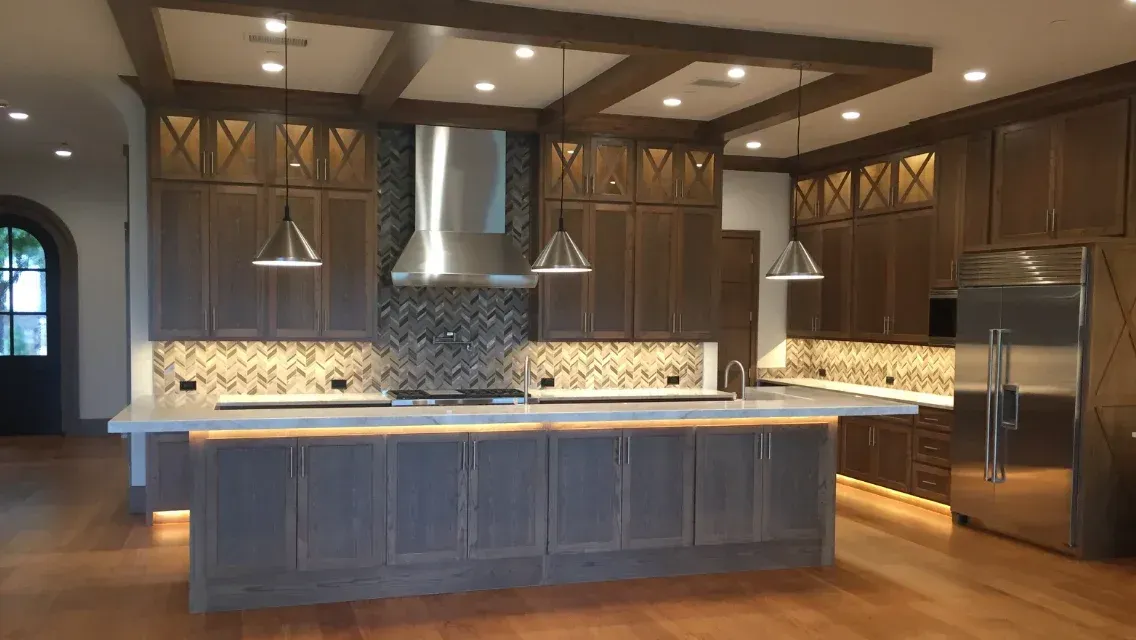 A spacious kitchen with dark wood cabinets, stainless steel appliances, a large center island, and herringbone tile backsplash.
