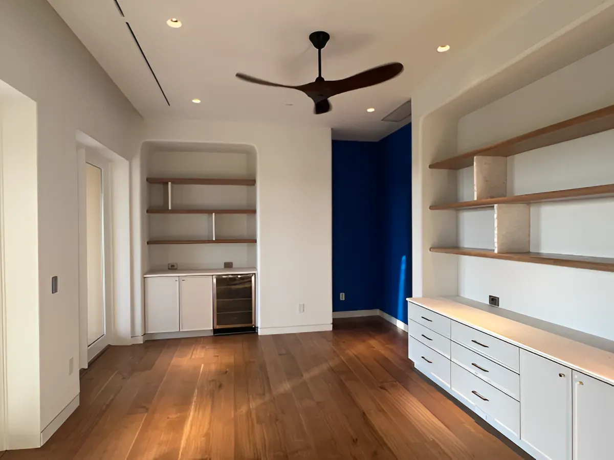 A modern interior room with white cabinetry, wooden shelving, dark blue accent walls, and a ceiling fan over hardwood.