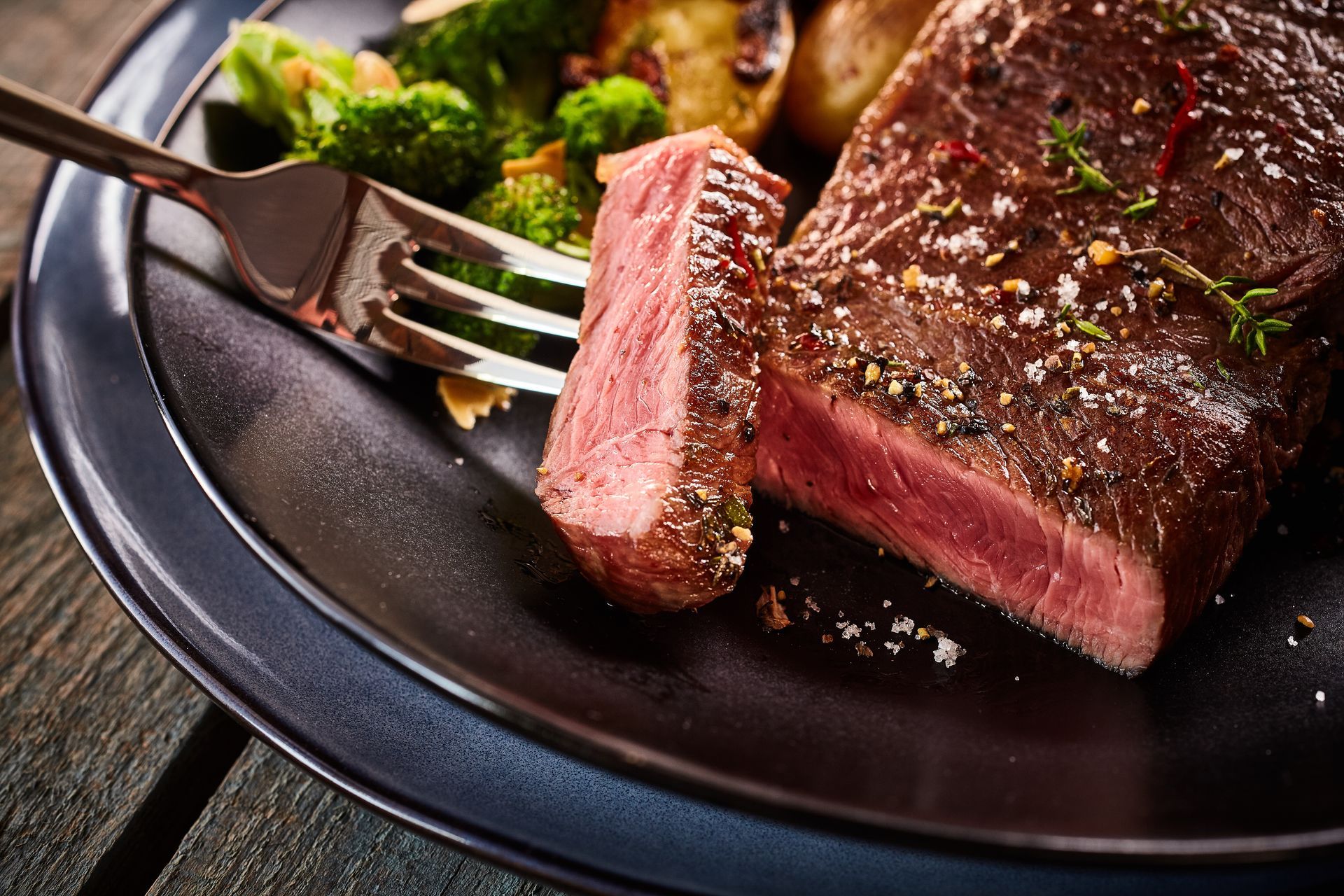A steak and broccoli on a black plate with a fork.