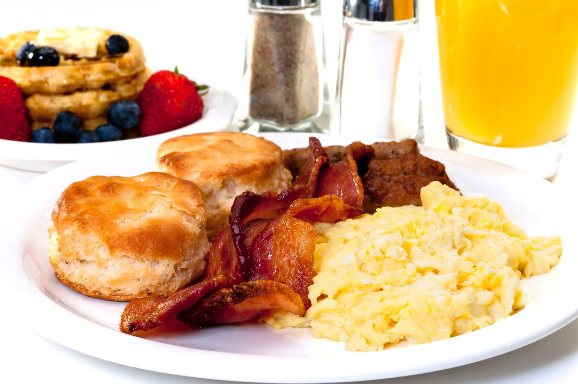 A white plate topped with scrambled eggs bacon and biscuits