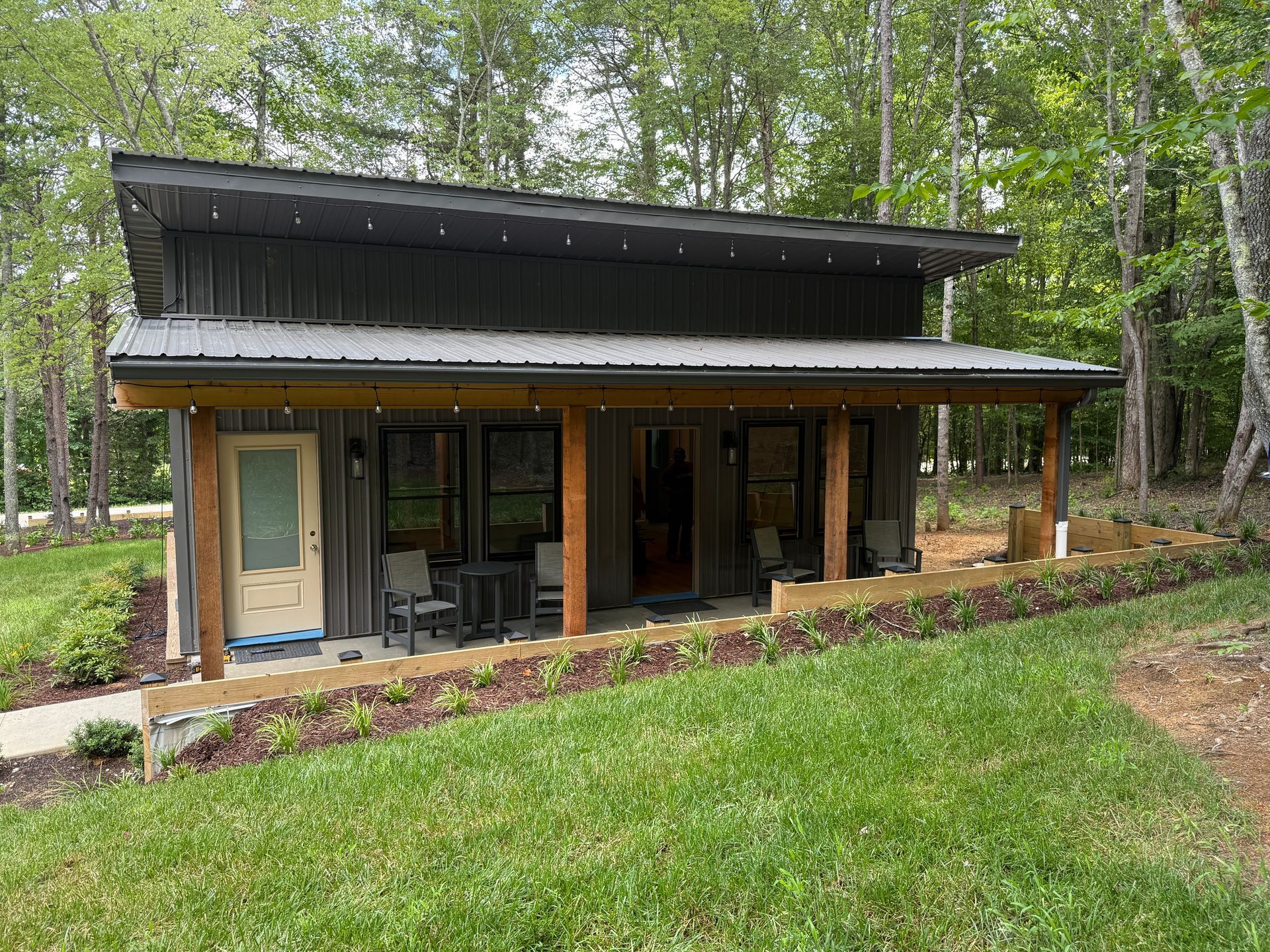 A small house with a porch in the middle of a lush green field.
