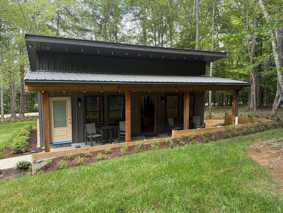 A small house with a porch in the middle of a lush green field.