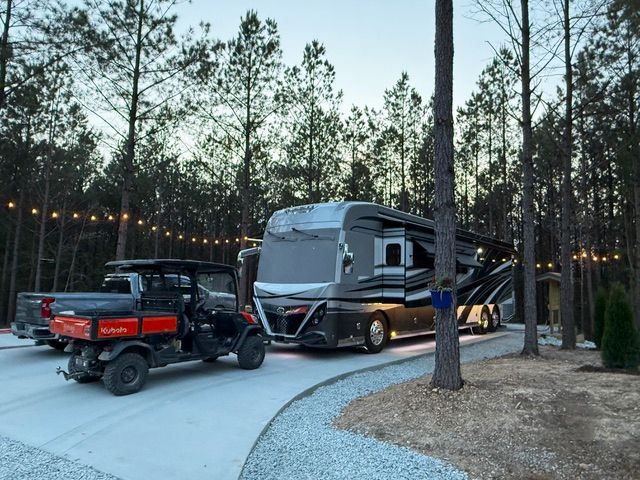 RV and utility vehicle parked on a gravel drive in a pine forest, strung with lights.
