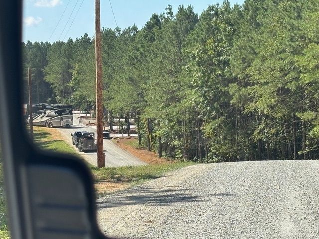 A car is driving down a gravel road next to a forest.