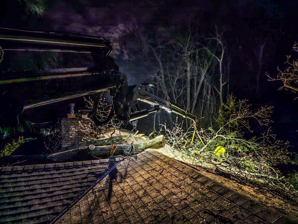 Night shot of a damaged house with a tree fallen on the roof.