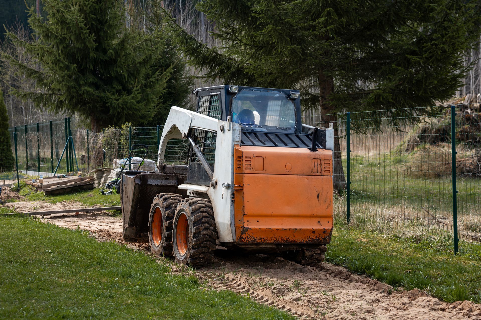 An orange skid steer loader placing tree branches and logs into a black dump truck on a rural road An orange skid steer loader placing tree branches and logs into a black dump truck on a rural road