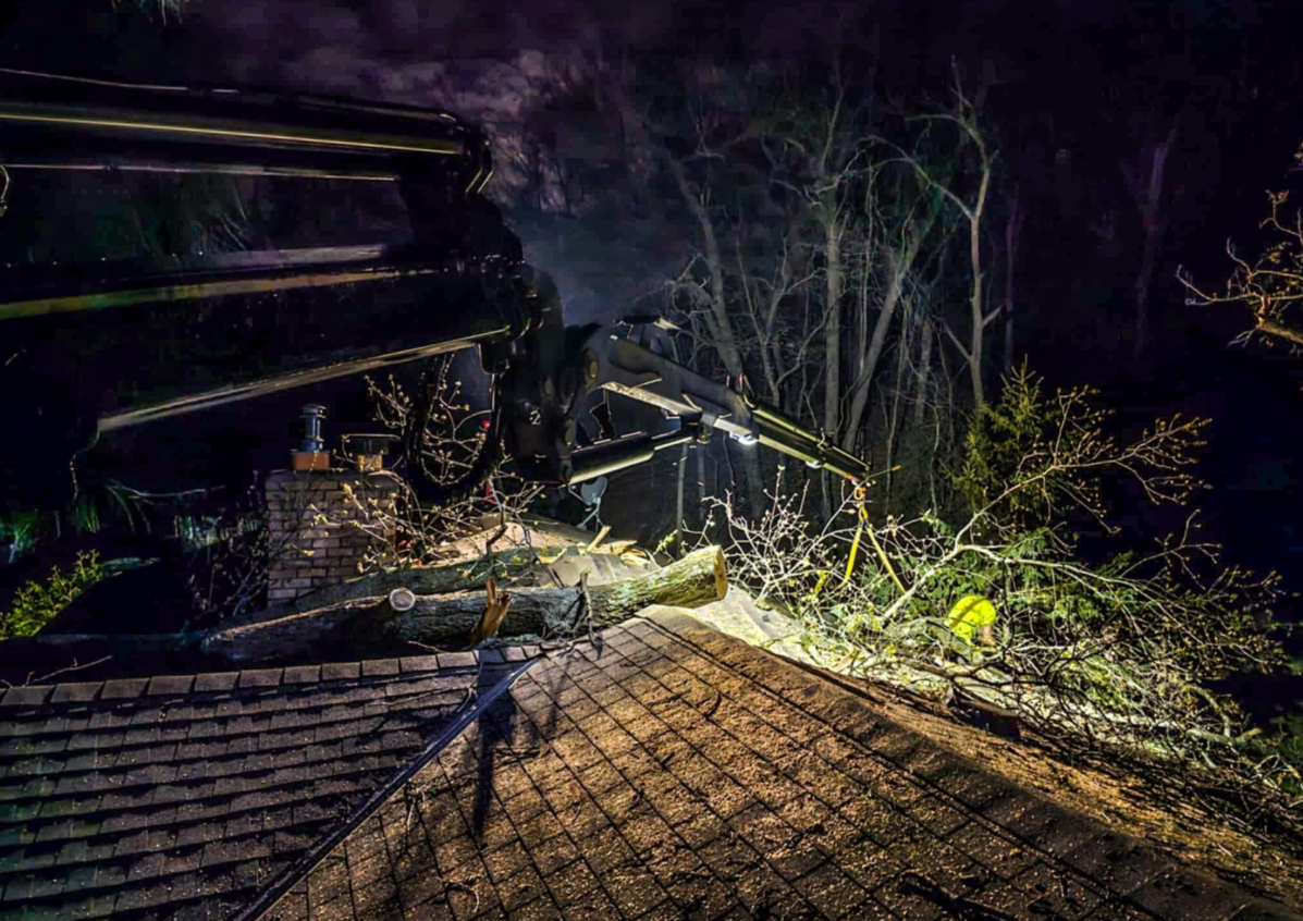 Rooftop damage: tree debris and collapsed roof at night. Dark scene, possibly storm-related.