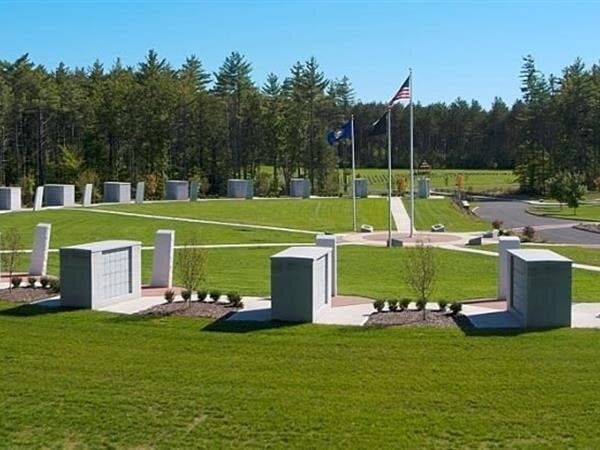 Veterans memorial with white rectangular monuments, flags, and green grass.