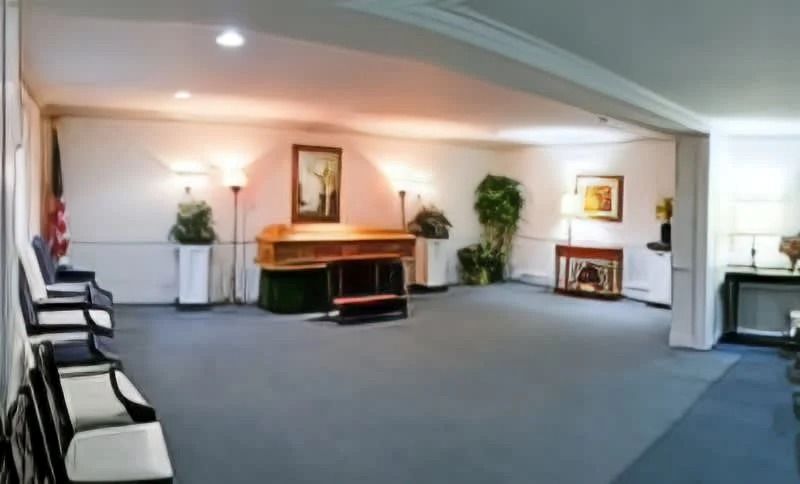 Funeral home interior with a casket, chairs, and a fireplace.