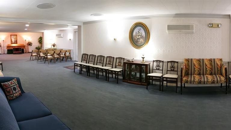 Funeral home interior with blue carpet, white walls, chairs, and a sofa.