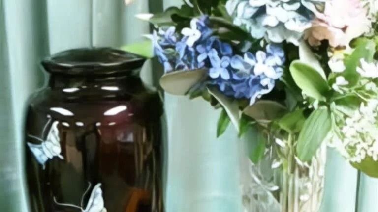 Dark urn with butterfly design next to a vase of blue and white flowers.