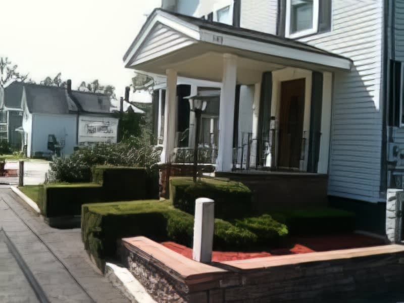 Front porch of a house with brick, manicured bushes, and a black walkway.