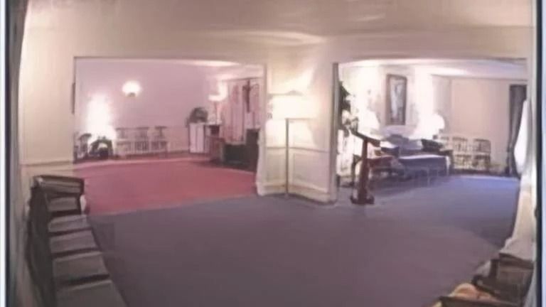 Interior of a well-lit room, showing doorways leading to other rooms. Blue and red carpet, furniture, chairs.