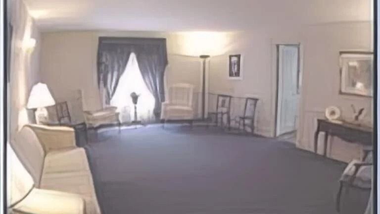 A funeral home visitation room with dark carpet, chairs, and a window with dark curtains.
