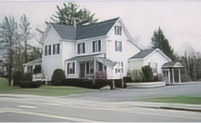 White two-story building with black shutters, a small porch, and a curved driveway.