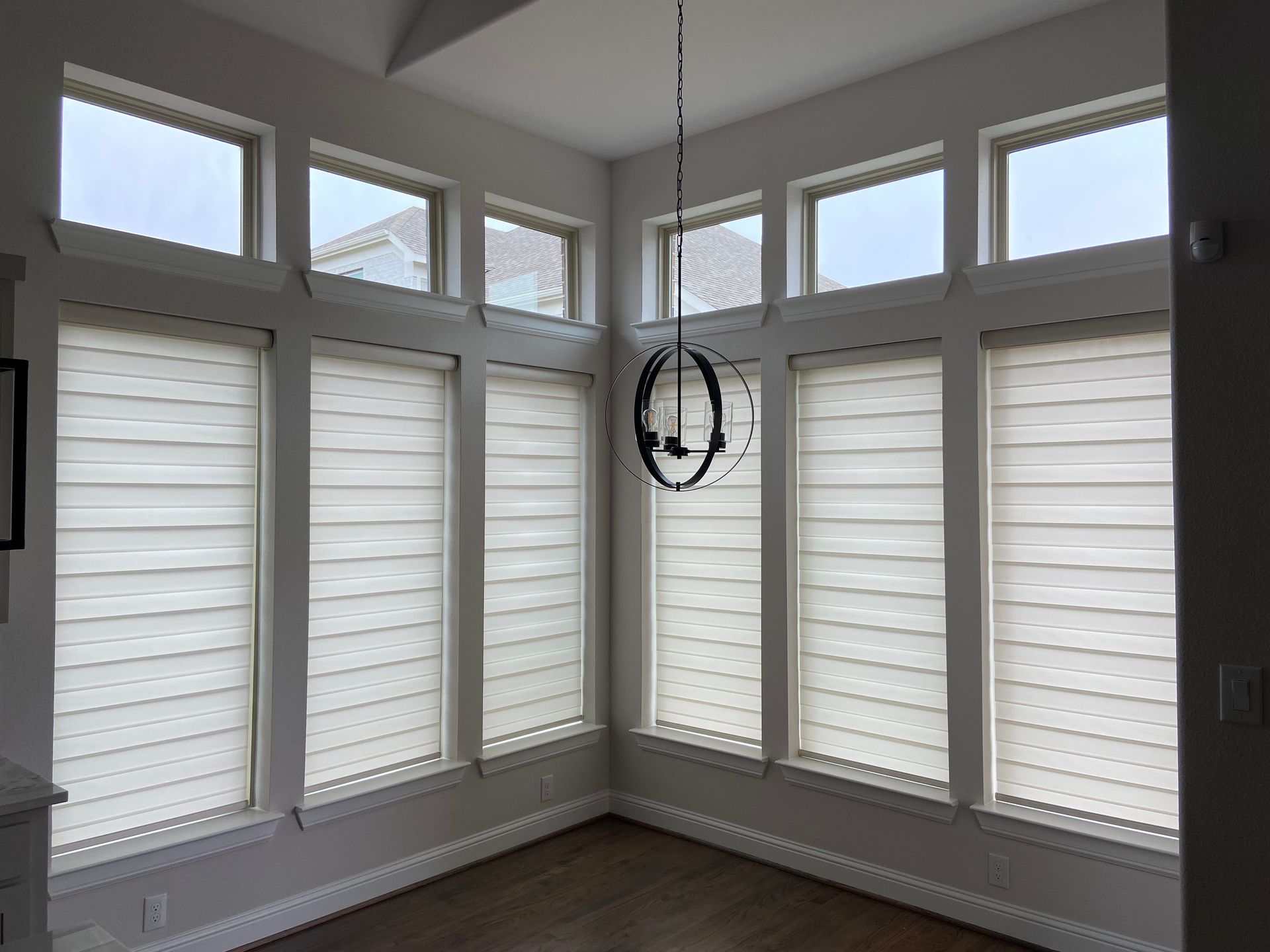 Room corner with large windows, light-colored blinds, and a hanging light fixture.
