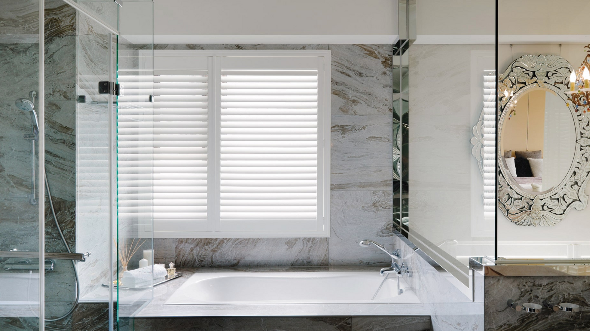 Bathroom with tub and shower, marble walls, window with shutters, decorative mirror.