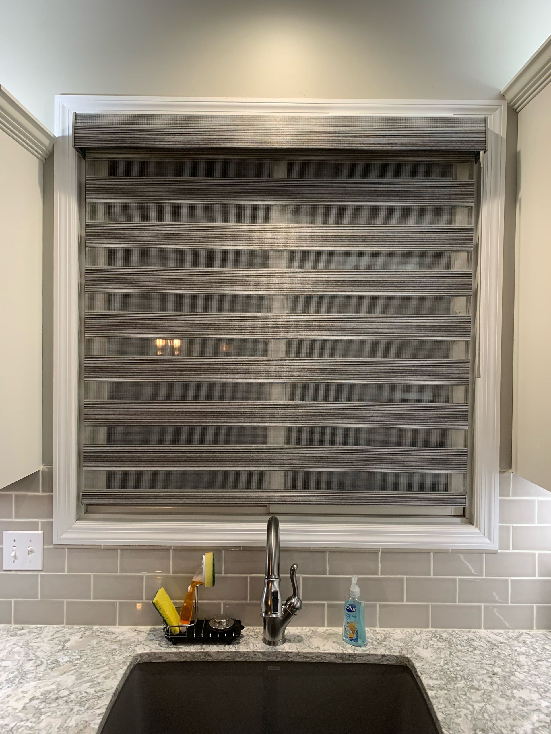 Kitchen sink with patterned window blinds. Gray and white color scheme.